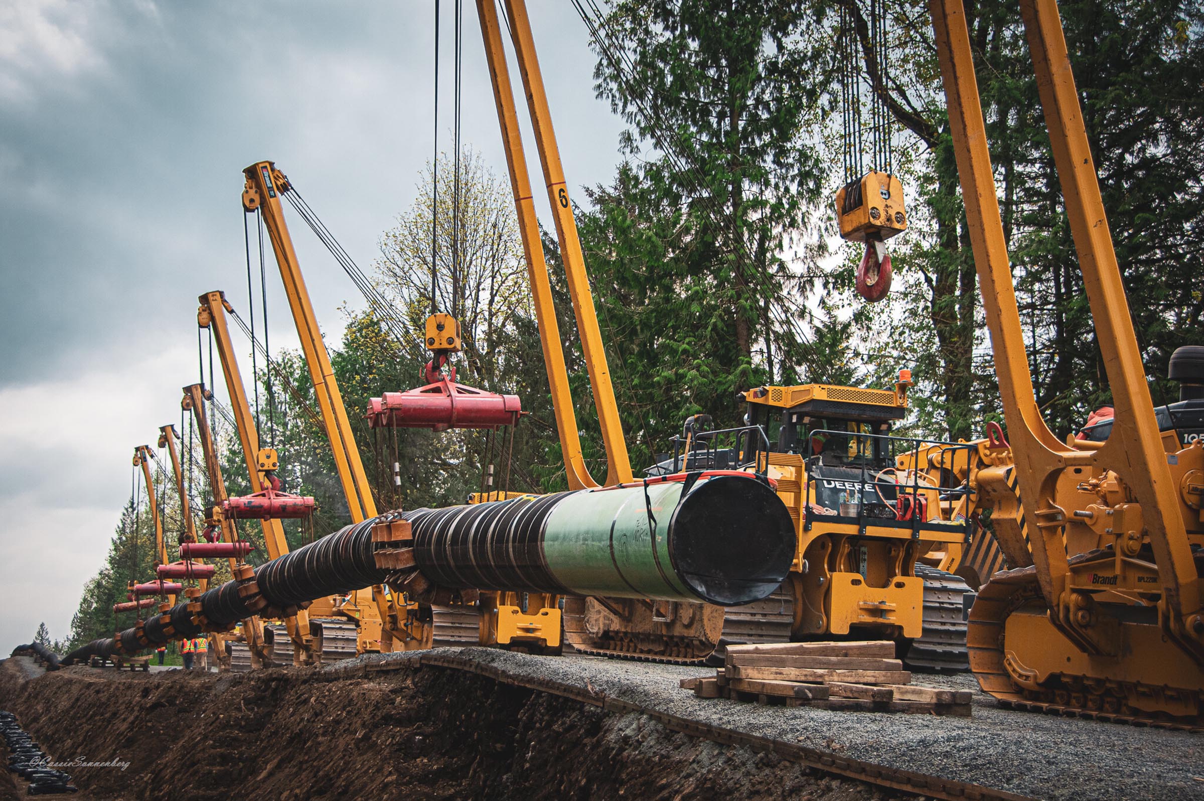 large machines laying sections of pipeline in a trench